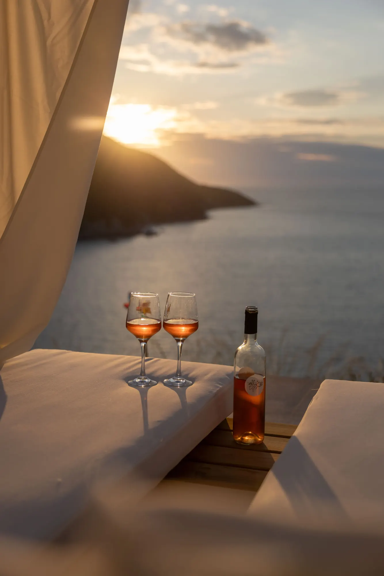 Two glasses of rosé on a daybed at sunset over the Ionian Sea